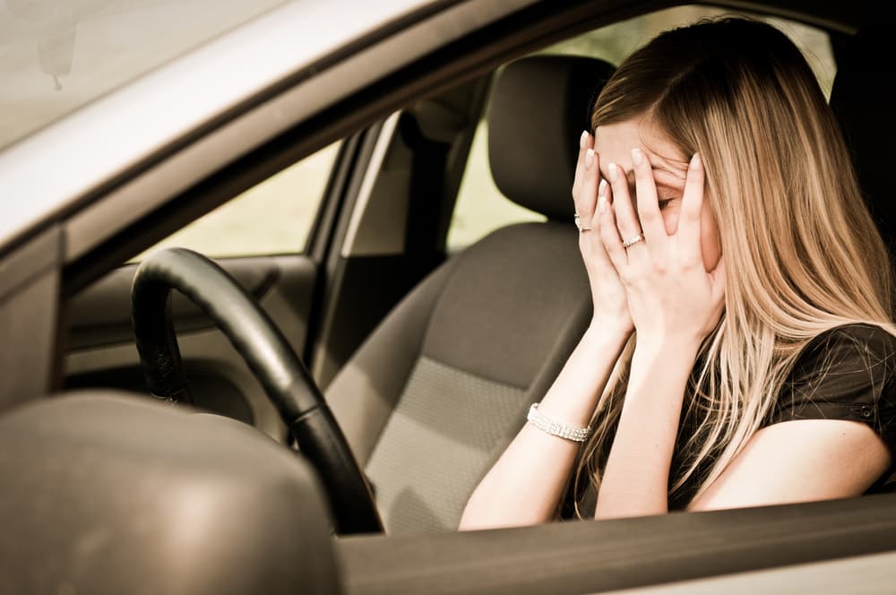  A young woman sitting in a car after a car accident, looking distressed with her hands covering her eyes, highlighting the emotional impact of the incident.