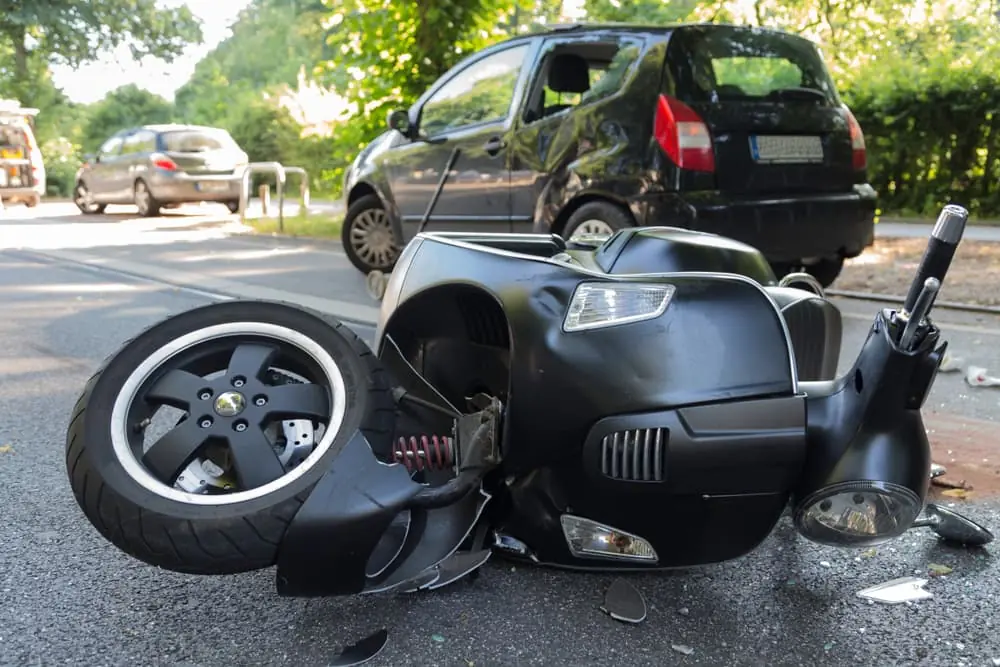 Motor scooter accident with a car on a busy road.