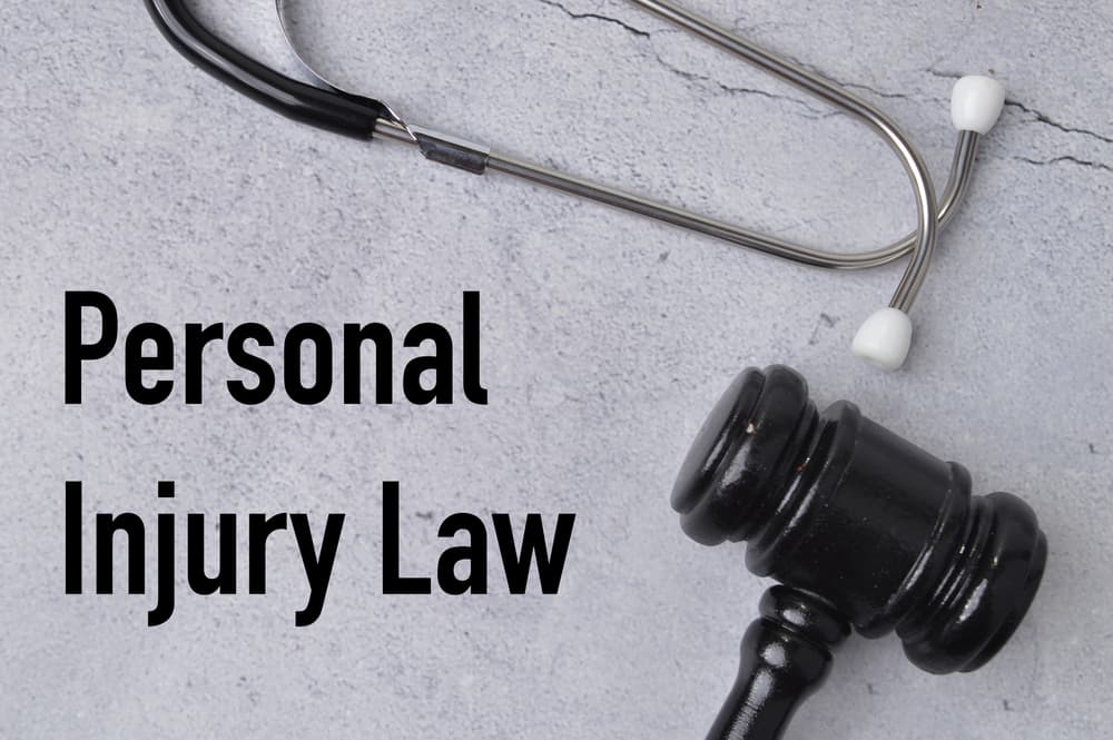 Top view of a stethoscope and judge's gavel on a grey background with the text "PERSONAL INJURY LAW."