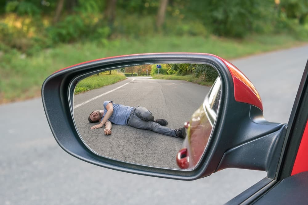 Hit-and-run scenario: A reflection in a car's rearview mirror shows an injured man lying on the road.