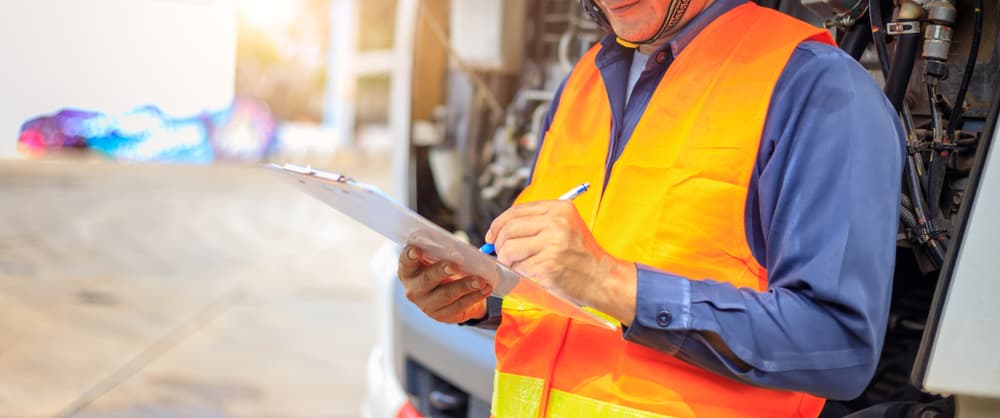 Close-up of an insurance agent taking notes on a clipboard while evaluating a truck after an accident.