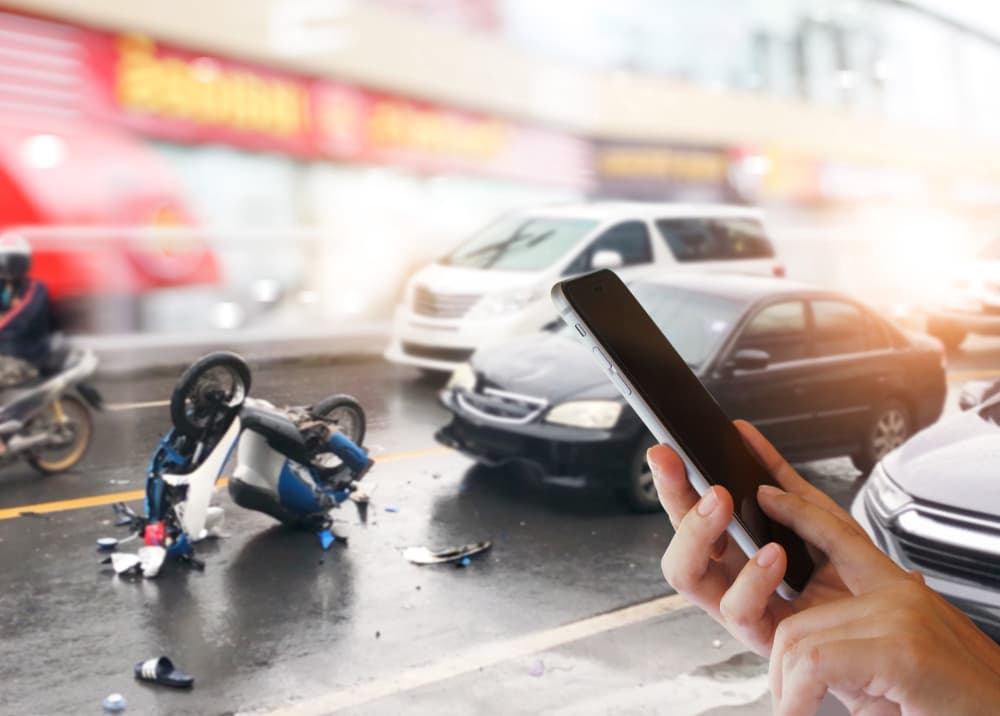 In heavy traffic, a careless driver collides with a motorcycle. A woman uses her smartphone to call for an ambulance and contact insurance company.




