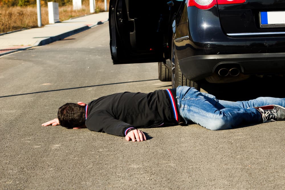 A man lies on the road behind a black car after a collision, with the pedestrian on the ground following the accident.