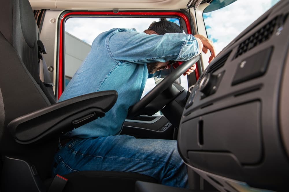 A side view of a truck driver holding his head in pain, visibly distressed, after experiencing a truck accident.